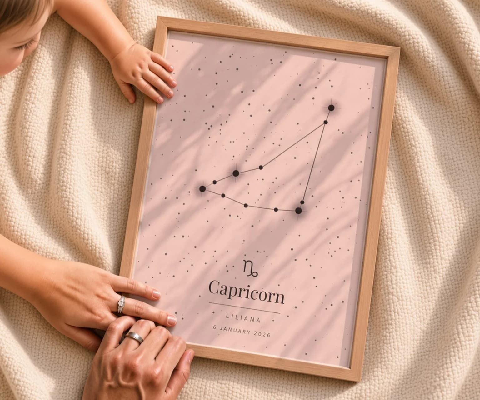 L'affiche du signe Capricorne, encadrée en chêne, posée sur une couverture entre les mains des parents et celle du bébé